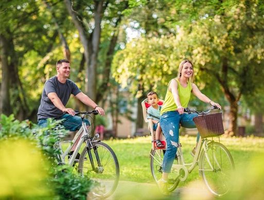 A white family ride bikes in a park