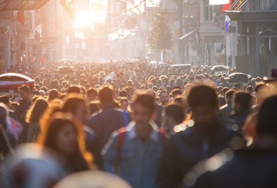 A crowd of people walking down a busy street with the sun behind them