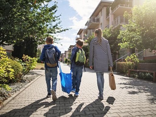 Two young boys carry a plastic bag down a street with their mother
