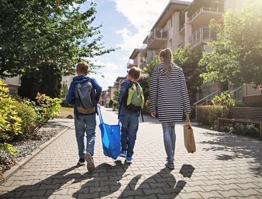 Two young boys carry a plastic bag down a street with their mother