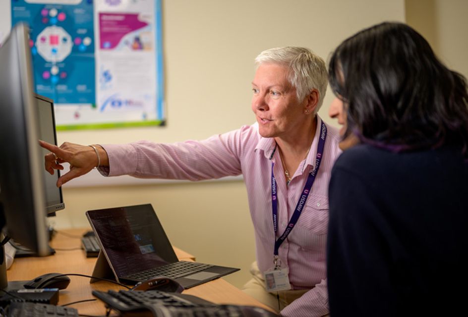 A white older woman with short white hair pointing to something on a computer screen in an office.