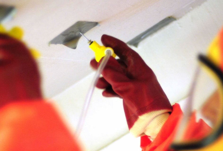 A person in a hazmat suit testing a ceiling for asbestos using tubes.