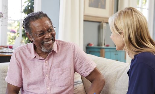 Smiling man talking with a woman during a relaxed conversation in a cozy, well-lit living room.