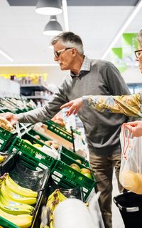 An older white couple picking out fruit and vegetables at a supermarket.