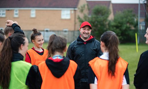 A football coach talks to a football team made up of young girls.