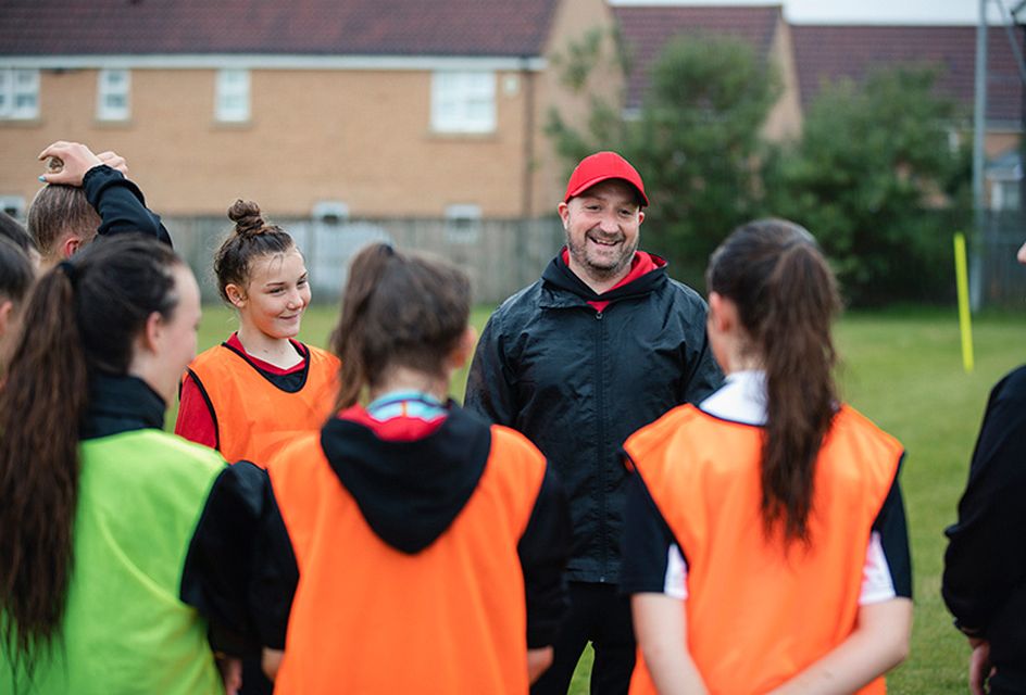 A football coach talks to a football team made up of young girls.