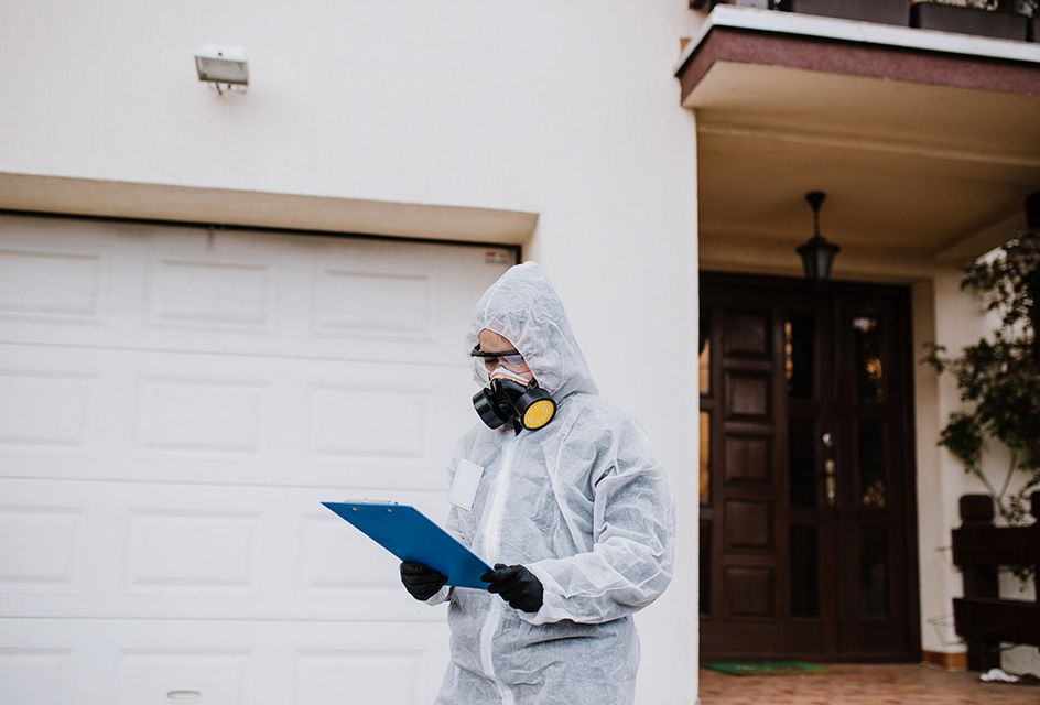 A person in a hazmat suit and respirator looking at a clipboard