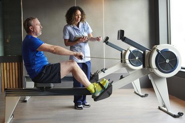 Female physical therapist helping a male patient to use an exercise machine