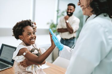 A young child high-fiving a doctor after receiving a vaccination