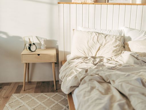 An empty unmade bed with an alarm clock next to it.