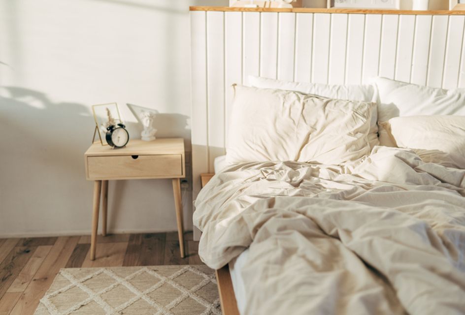 An empty unmade bed with an alarm clock next to it.