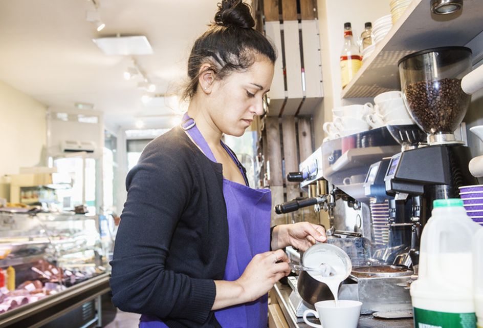 A female barista pours milk into a cup in a cafe.