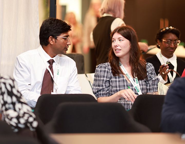 A man and a woman talking at a conference. They both wear RSPH lanyards.