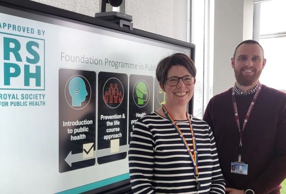 Two people stand beside a screen displaying "Foundation Programme in Public Health" and the Royal Society for Public Health approval logo.