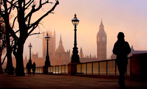 The houses of parliament pictured on a foggy winter morning from the Southbank. Ornate streetlights on railings to the Thames in shot as well as tree with no leaves.