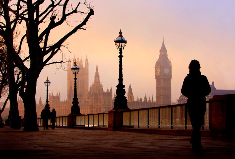 The houses of parliament pictured on a foggy winter morning from the Southbank. Ornate streetlights on railings to the Thames in shot as well as tree with no leaves.
