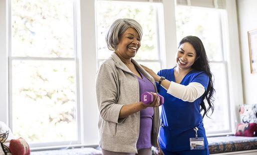 Smiling older woman doing physical therapy exercises with female physiotherapist at home