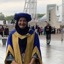 Saima Nafis, wearing purple and yellow PhD robes outside a graduation ceremony.