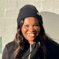 Uchenn Anderline Onu, a young black woman with long brown hair wearing a black hoodie and black beanie, smiling at the camera.