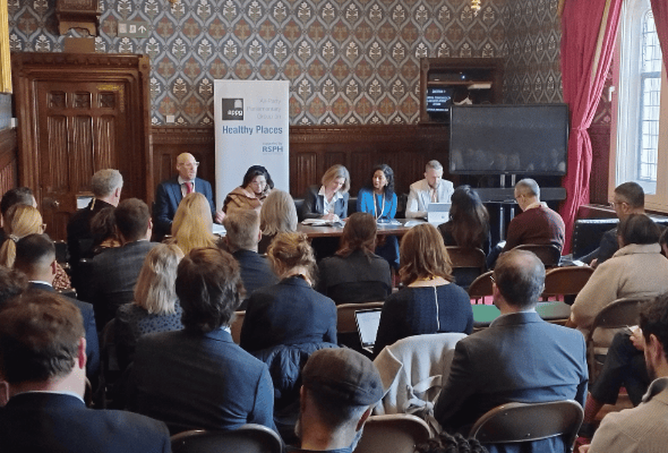 Panel discussion in a room in the houses of parliament with patterned wallpaper and red curtains.